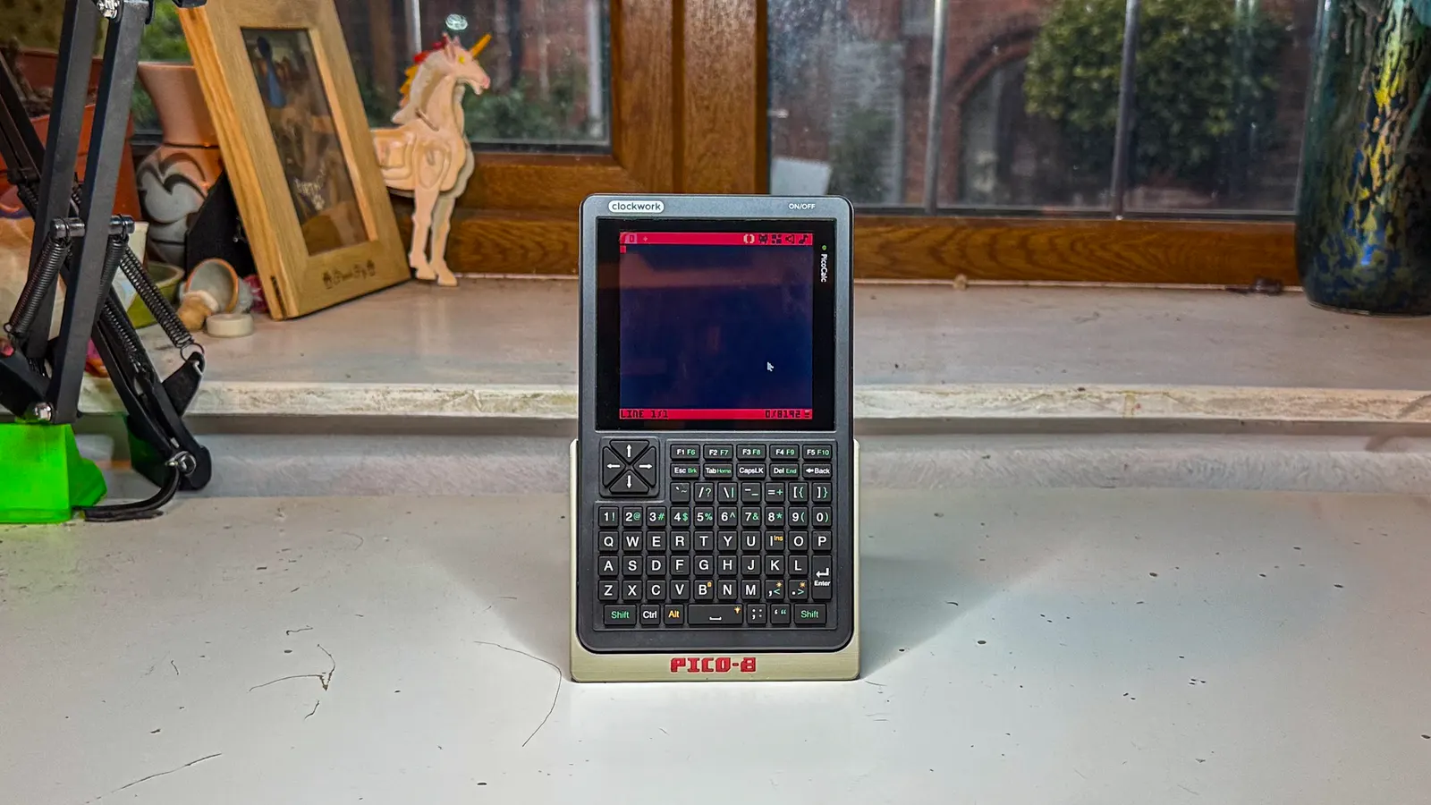 A ZeroCalc standing upright in a printed stand on a windowsill, showing the Pico-8 editor.